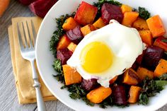 a white plate topped with vegetables and an egg on top of it next to a fork