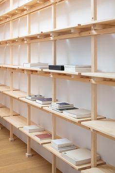 books are lined up on wooden shelves in a room with white walls and wood flooring