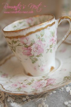 a cup and saucer sitting on top of a lace covered tablecloth with pink flowers