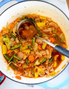 a pot filled with soup and vegetables on top of a stove burner next to a spoon