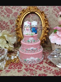 a hello kitty wedding cake is displayed in front of a mirror and vase with flowers