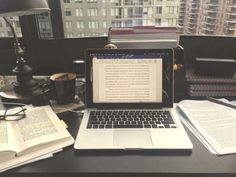 an open laptop computer sitting on top of a desk next to a book and coffee cup