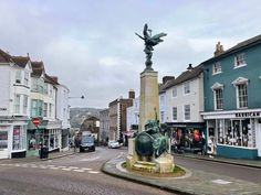 there is a statue in the middle of the street with buildings around it and shops on both sides