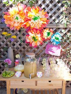 there is a table with flowers and drinks on it in front of a wooden fence