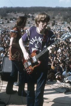 two young men playing guitars in front of an audience