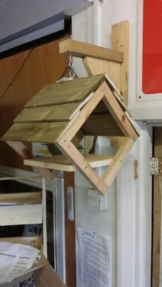 a bird house hanging from the side of a wall next to a box filled with wood