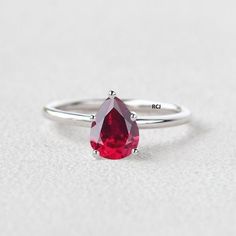 a close up of a ring with a pear shaped red stone on it's side