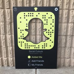 a black and yellow sign with a snapchat on it's side next to a brick wall