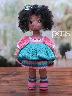 a doll with curly hair wearing a dress and boots on a wooden table in front of a window