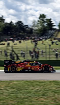 a red and yellow race car driving on a track with people watching from the sidelines