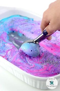 a person using a spatula to dip purple and blue paint in a white container