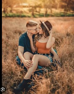 a man and woman sitting on the ground kissing in a field with tall brown grass