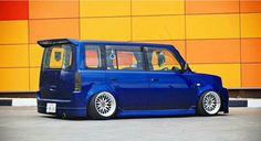 a blue mini van parked in front of a building with orange and yellow walls behind it