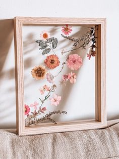 a wooden frame with flowers and leaves on the wall next to a pillow, in front of a white wall