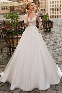 a woman in a white wedding dress standing on a cobblestone street with buildings behind her