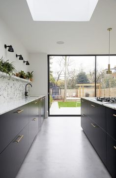 an open kitchen with black cabinets and marble counter tops is seen from the hallway leading to the backyard