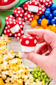 a hand is holding a small red mushroom in front of some colorful candy candies