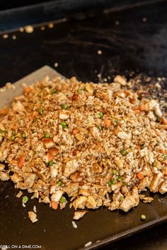 a pile of food sitting on top of a black tray next to a pan filled with rice