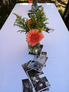 an arrangement of flowers in a vase on a long table with photos pinned to it