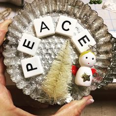 a person holding a christmas ornament with the word peace spelled on it