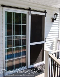 an open screen door on the outside of a house with white siding and black shutters