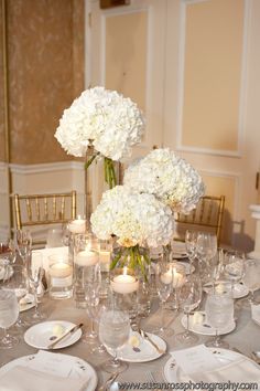 a table with white flowers and candles is set for a formal dinner or reception in an elegant setting