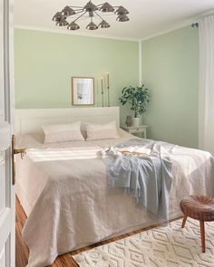 a bedroom with green walls, white bedding and an area rug on the floor