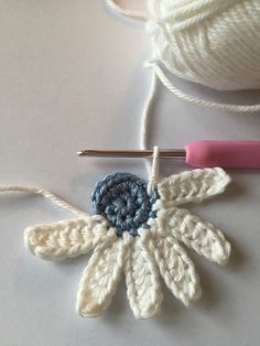 a crochet flower is next to a ball of yarn and a knitting needle