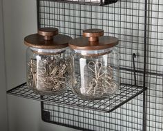 two glass jars with wooden lids are sitting on a wire shelf