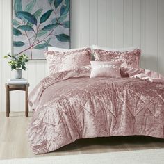 a bed with pink comforter and pillows in a room next to a painting on the wall