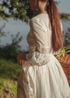 A dreamy ivory dress with floral embroidery on the net inserts, in tiers and shoulders. The tiny details in this dress are a delight. This dress is full length, buttons in front, also has a smocking detail on the waist. The romance of this dress comes to life with pink and sage flowers embroidered on the up-cycled net, the light weight cotton will make you feel like you're walking on clouds. IMPACT & CARE Made from upcycled materials Ethically made in Jaipur Hand wash in cold water FIT Your perf Spring Cottagecore Dress With Smocked Cuffs, White Feminine Prairie Dress For Garden Party, Feminine White Prairie Dress For Garden Party, Cottagecore Floral Embroidery Dress For Daywear, Bohemian Dresses With Smocked Cuffs For Garden Party, Delicate White Dress For Daywear, Spring White Maxi Dress For Gatherings, White Spring Maxi Dress For Gatherings, White Maxi Dress For Spring Gatherings