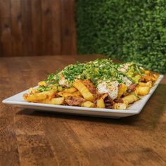 a white plate topped with lots of food on top of a wooden table next to a green plant