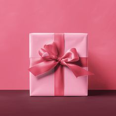 a pink gift box with a red bow on it sitting on a table against a pink background