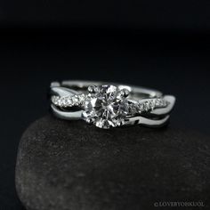 a white gold engagement ring with two diamonds on top of it, sitting on a rock