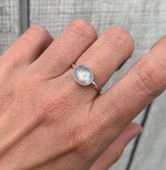 A beautiful luminescent white oval moonstone has been horizontally set in sterling silver with a handmade ring band from sterling silver half dome wire. The white moonstone changes colors when the light hits it going from a crisp white to having hues of blue, orange, or pink. The stone is 10mm x 8mm in size.  Made to order, please specify size when ordering! Each moonstone will vary in color, hues, and inner texture. If you would like to see the available moonstones, just ask! Moonstone is also White Moonstone Opal Ring In Oval Cabochon Shape, Minimalist White Moonstone Ring In Sterling Silver, Minimalist Oval Cabochon Opal Ring, White Opal Ring With Oval Cabochon Shape, Adjustable Minimalist Moonstone Ring In Sterling Silver, Minimalist Oval Opal Ring, Minimalist Adjustable Sterling Silver Moonstone Ring, Modern Oval Moonstone Jewelry, Minimalist Round Cabochon Moonstone Ring