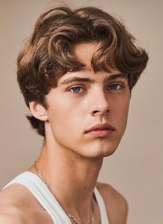 a young man wearing a white tank top looking at the camera with a serious look on his face