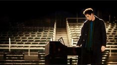 a man standing next to a piano in front of an empty bleachers