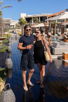 a man and woman standing next to each other on a wooden deck near the ocean