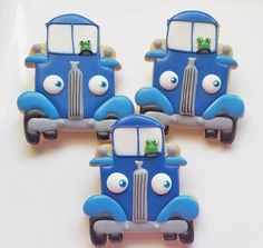 three blue trucks with googly eyes are sitting on a white surface and one has a green frog in the front