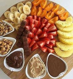 a variety of fruits, nuts and chocolate on a wooden platter with dips