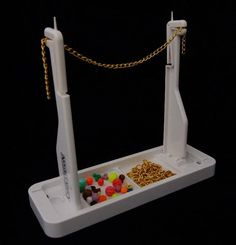 a white plastic object with gold chains and candy in it's tray on a black background