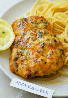 a white plate topped with chicken and pasta next to a lemon wedge on top of a table