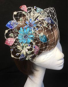 Delicate glass resin floral fascinator perfect for the guest who wants something unique and stunning. This design is a beautiful selection of glass effect leaves and flowers teamed with crystal swirls and set onto a fine base tiara band with a soft veiling finish. As with all our designs, this piece can be made exact to the image or in any colour combination to match in with your outfit. If a specific colour is required customers can message over an image of their outfit and accessories, or if t Whimsical Flower Fascinator For Parties, Handmade Whimsical Fascinator For Party, Whimsical Flower Headpieces For Wedding, Whimsical Blue Adjustable Headpiece, Whimsical Flower Wedding Headpieces, Whimsical Handmade Party Fascinator, Blue Adjustable Whimsical Headpiece, Handmade Whimsical Party Fascinator, Whimsical Blue Fascinator For Party