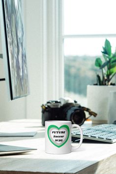 a white coffee mug sitting on top of a desk next to a keyboard and monitor