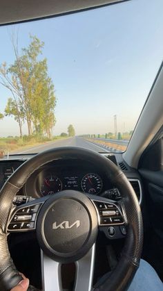 the steering wheel and dashboard of a car on a road with trees in the background