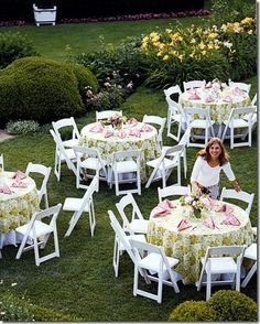 a woman standing next to a bunch of white tables and chairs in the grass with flowers on them