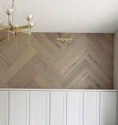 an empty room with white cupboards and wood wallpaper on the walls, along with a chandelier