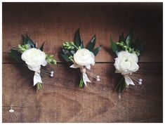 three bouquets of white flowers are arranged on a wooden surface with greenery and leaves