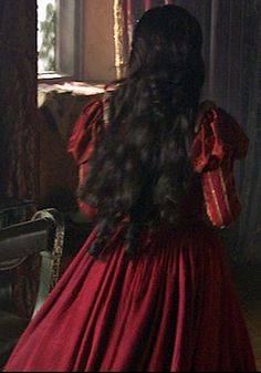 the back of a woman's head in a red dress looking out a window