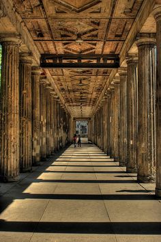 the inside of an old building with columns and people walking down one side in the distance